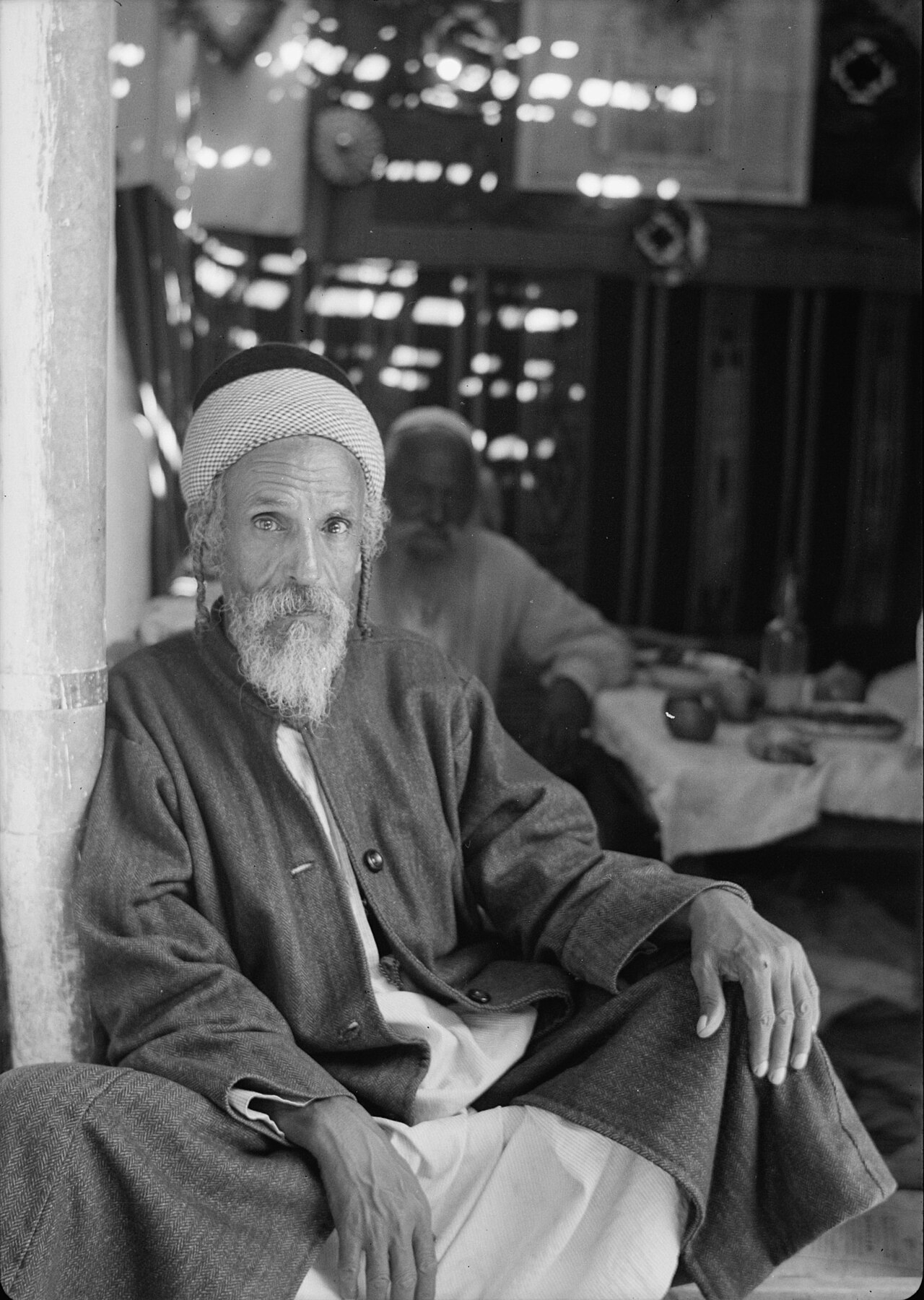 A period photograph of a man seated in the doorway of a sukkah, a leafy booth built for the Feast of Tabernacles.