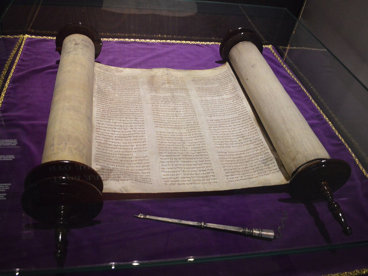 An open Torah scroll with columns of Hebrew text, wooden rollers at each side.